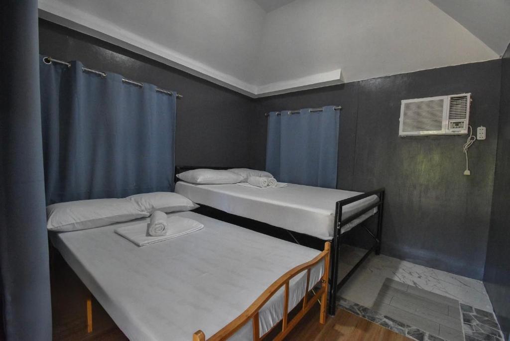 two beds in a small room with blue curtains at Ohana in Coron