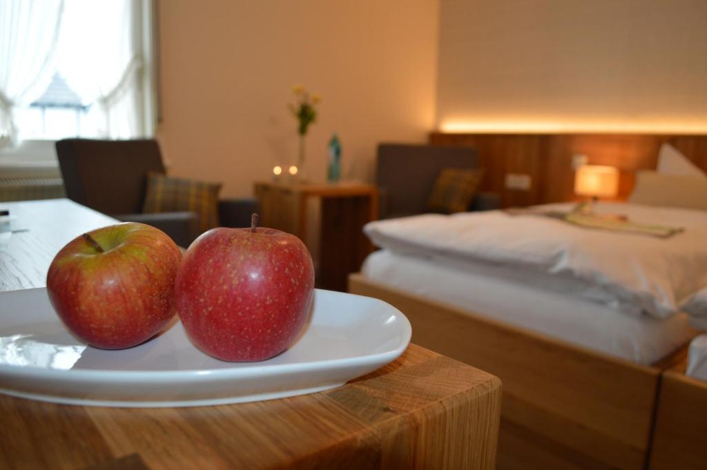 two apples on a plate on a table with a bed at Forellenhof Poggel in Eslohe