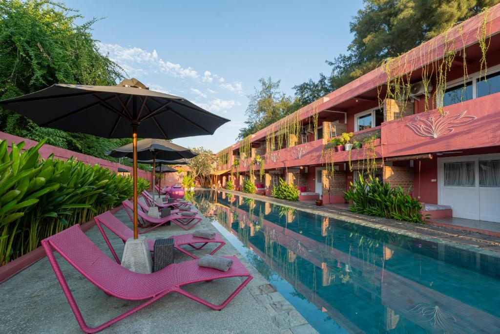 a pool with chairs and an umbrella next to a hotel at PinkCoco Gili Trawangan - Constant Surprises - for Cool Adults Only in Gili Trawangan