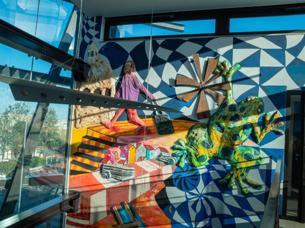 A glass-sided interior walkway featuring a large, colourful mural of a frog and Lisbon-inspired scenes.
