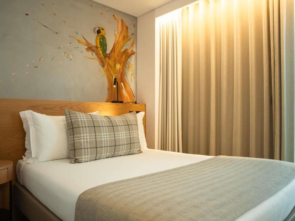A single bed with crisp white bedding, plaid cushions, a grey runner and a colourful bird mural.