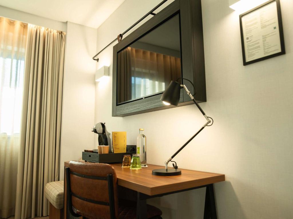 A compact wooden desk beside the window, equipped with a task lamp and coffee-making setup.