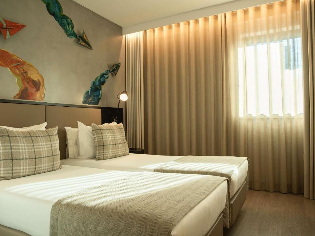 A twin bedroom with two single beds, a curtained window and colorful wall artwork.