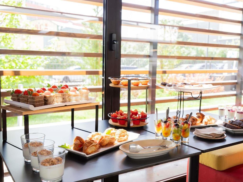 A bright breakfast buffet by large windows, featuring pastries, fruit, yogurt and small desserts.