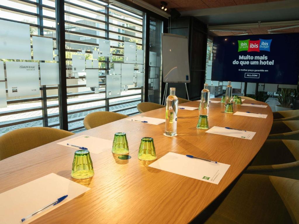 A conference table prepared with water, glasses, paper and pens beside tall windows.