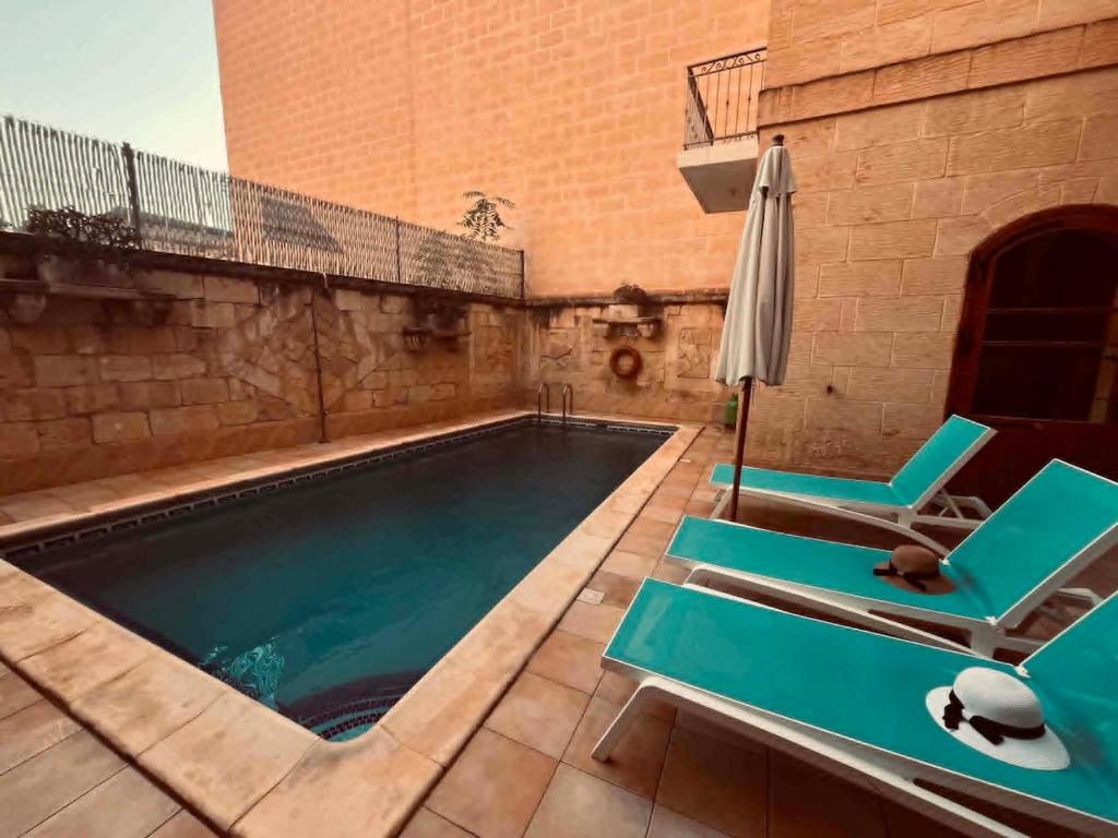 a swimming pool with two chairs and an umbrella at Il- Pellikan Farmhouse in Għajnsielem