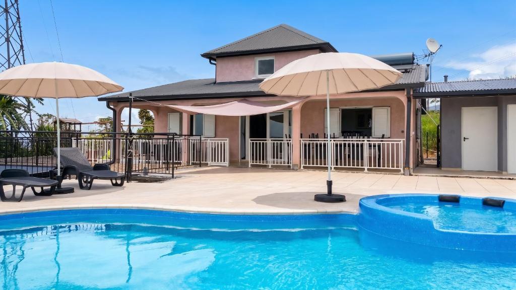 a house with a swimming pool and two umbrellas at Villa enchanteresse à Saint-Benoît avec piscine privée in Saint-Benoît