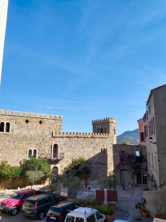 a large stone building with cars parked in a parking lot at Appartement charmant à Algajola avec terrasse in Algajola