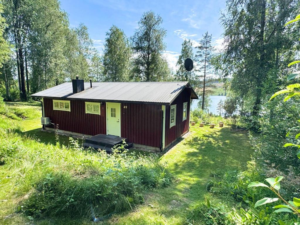 a small red cabin in a field with a lake at Hus Bjöksjöblick in Hällefors