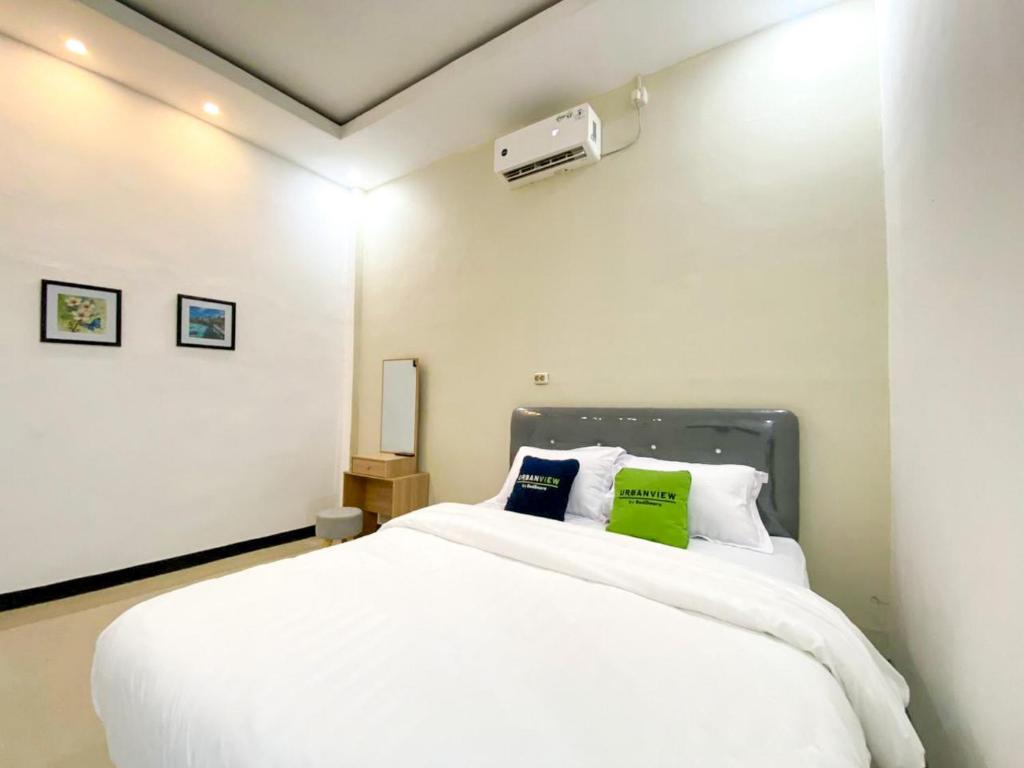 a bedroom with a white bed with two green pillows at Urbanview Bangsal Mojokerto in Ngranggon
