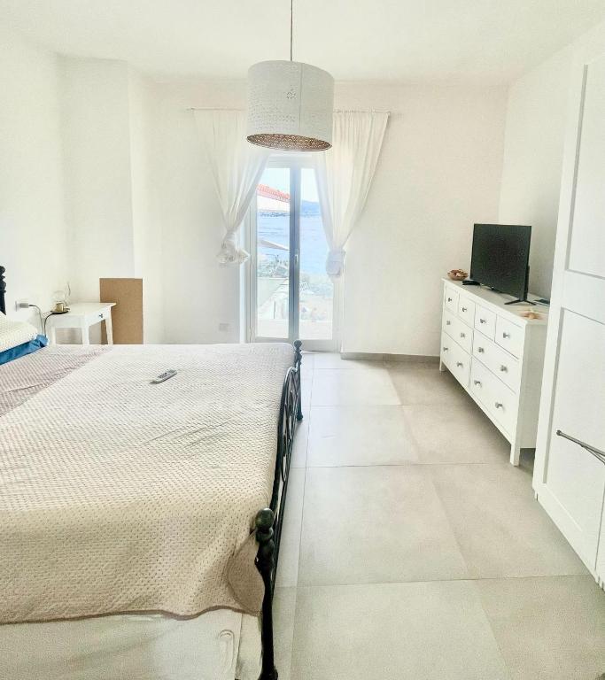 a white bedroom with a bed and a window at Casa Peloro in Torre Faro