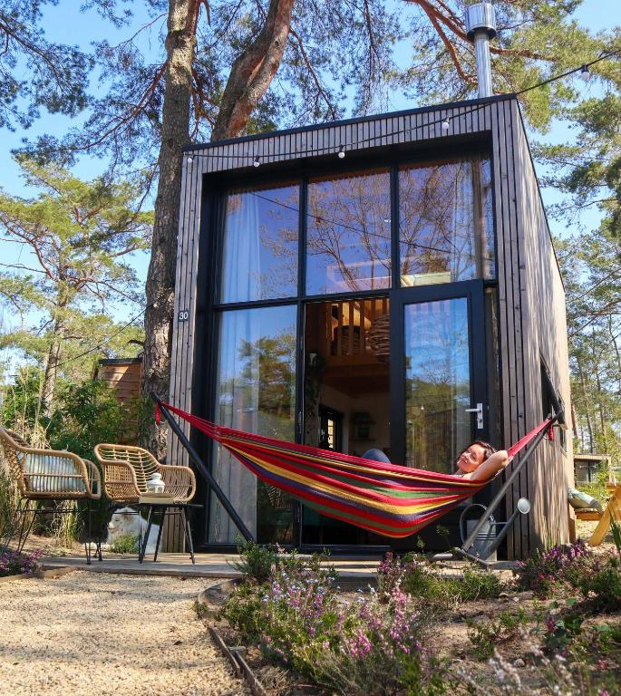 a person laying in a hammock in front of a house at Tiny House of Happiness - shared hot tub in Otterlo