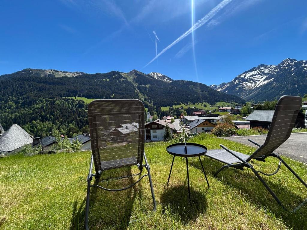 two chairs and a table on a field with mountains at Ferienwohnung Kleinwalsertal in Hirschegg