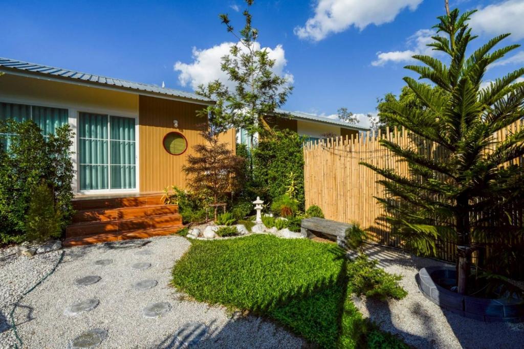 a garden with a yellow house and a fence at After Beach House Phla Resort in U-Tapao