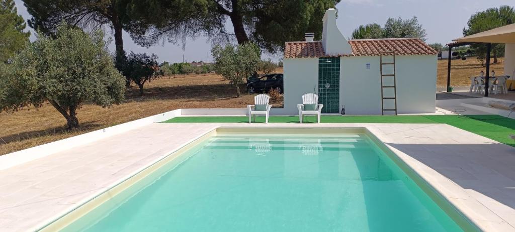 a swimming pool with two chairs and a house at Quinta Do Pinheirão in Coruche