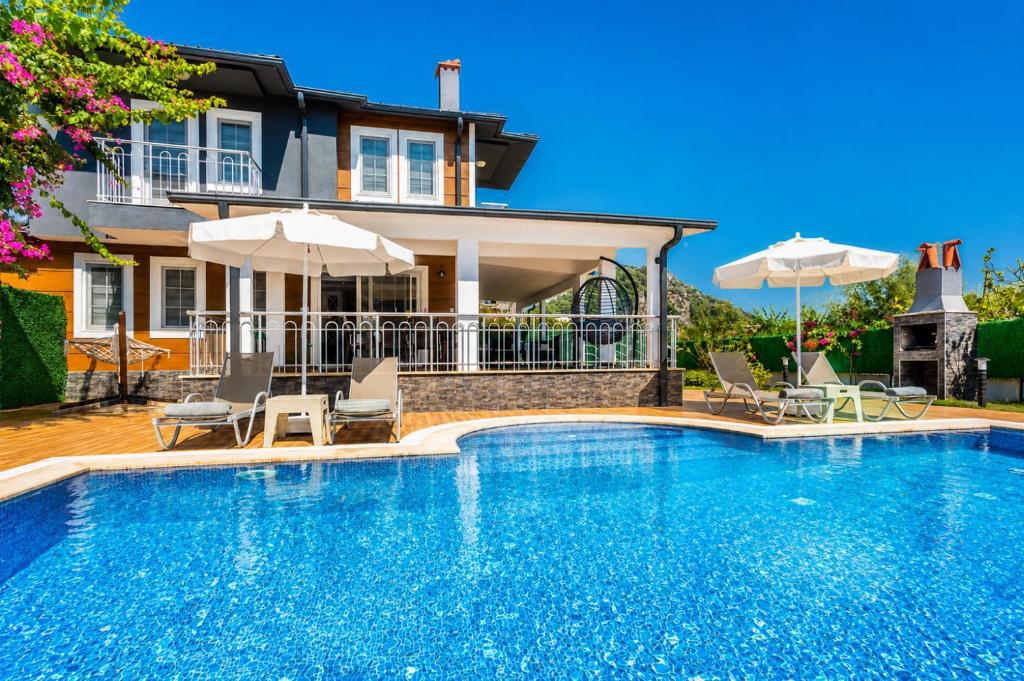 a swimming pool with chairs and umbrellas in front of a house at Villa Delfin in Ortaca