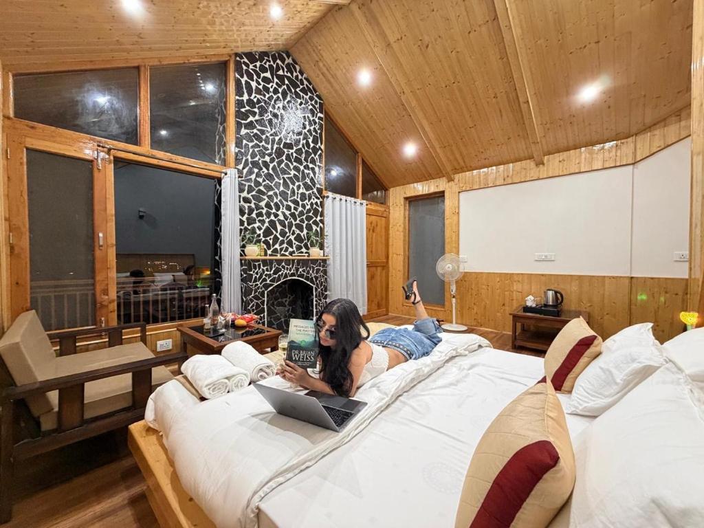 a woman laying on a bed with a laptop at Tirthan Wood , a river view cottage in Banjār