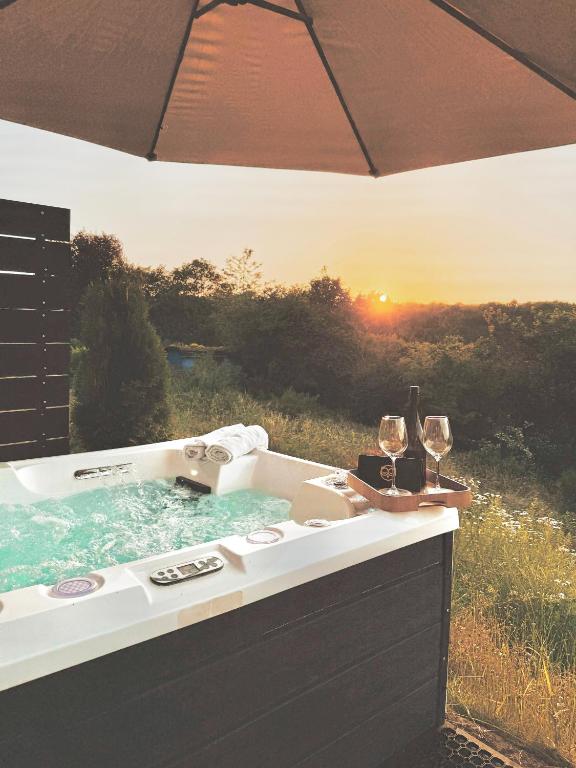 an outdoor hot tub with wine glasses and an umbrella at Tiny House mit Whirlpool und Sauna in Bermel