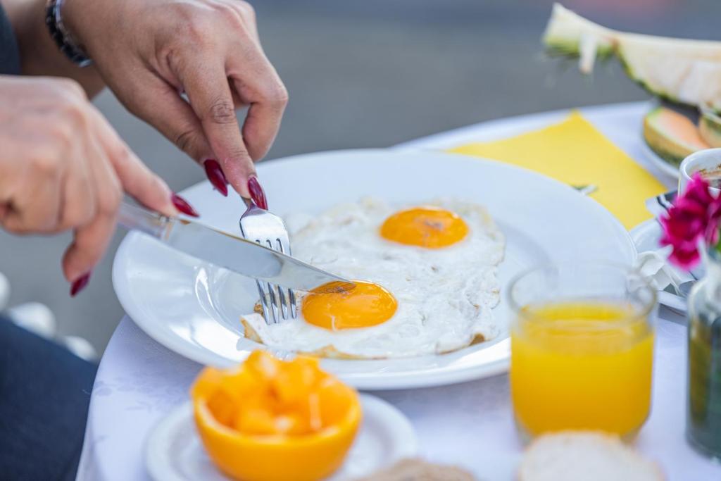 a person cutting an egg on a plate with a knife and fork at Hôtel des Roches Kourou in Kourou