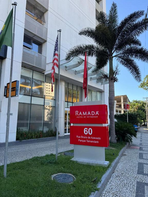 a sign in front of a building with a palm tree at Ramada Hotel & Suites Campos Pelinca in Campos dos Goytacazes