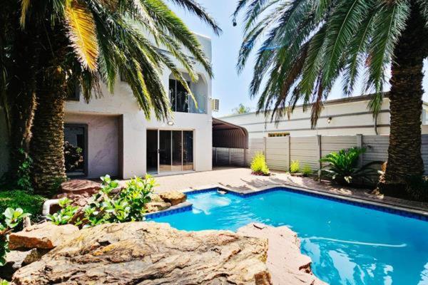 a swimming pool in front of a house with palm trees at Magic garden in Vereeniging
