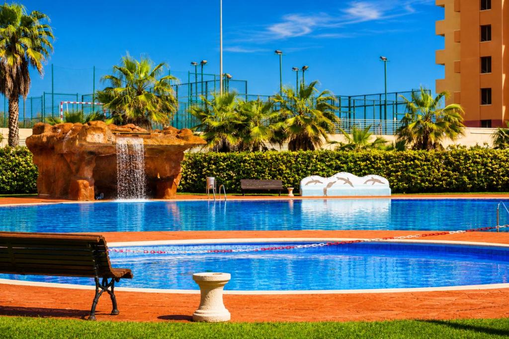 a swimming pool with a fountain and a bench at Los Juncos V Apartments in La Pineda