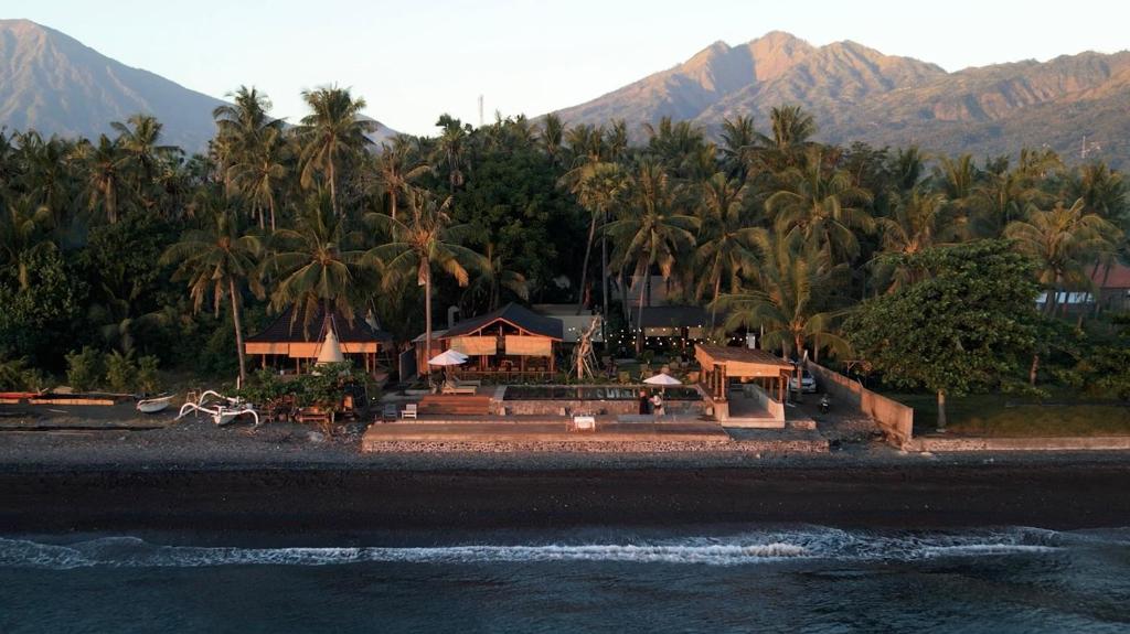 a resort with palm trees and mountains in the background at Vela Tianyar Boutique Resort - Oceanfront in Tianyar