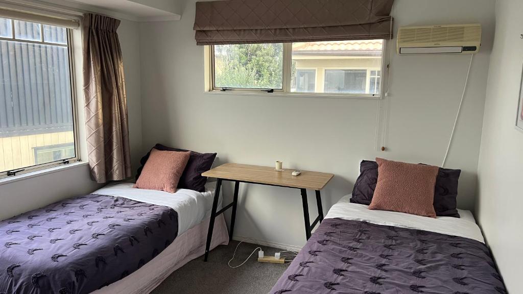 two beds in a room with a table and windows at Beachside Bliss in Tauranga