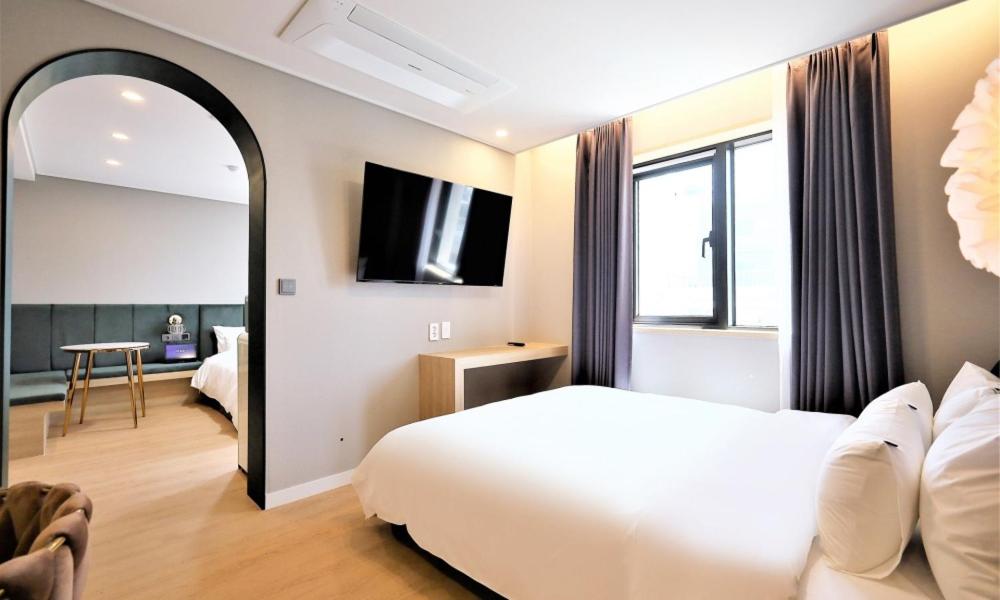 a hotel room with a white bed and a television at De Lamour Hotel in Tongyeong