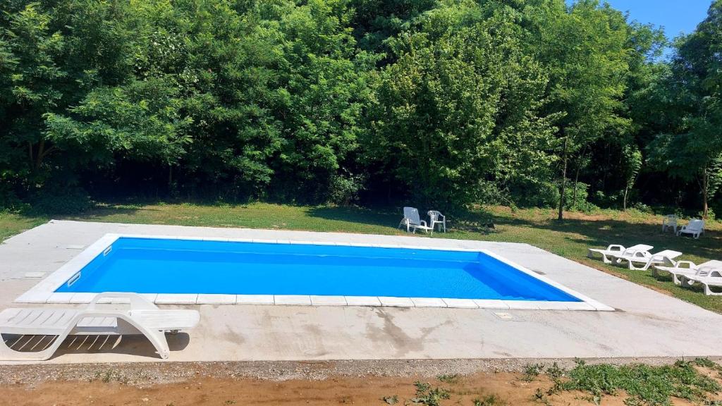 a blue swimming pool with two white chairs and trees at Farmica, Bed&Breakfast, Bazen izdvojen nekoliko minuta hoda in Ðurđevac
