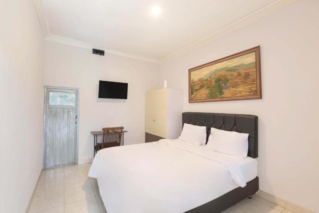 a bedroom with a white bed with a painting on the wall at Agni Homestay in Yogyakarta