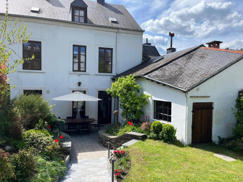 a white house with a table and an umbrella at Gîte L'Hôte-Antique in Bouillon