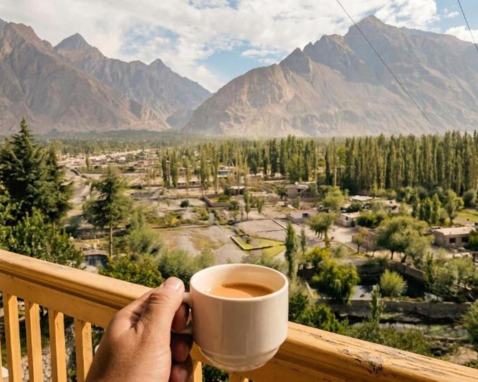 a person holding a cup of coffee on a balcony at Hotel Mashabrum Skardu Free Breakfast Mountain View Family Rooms & Free WiFi in Skardu