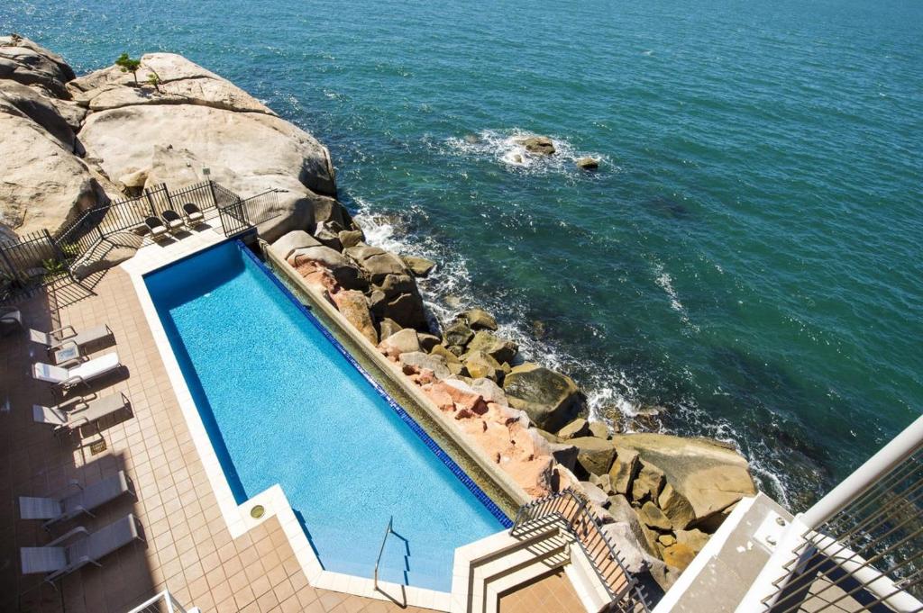 a swimming pool next to the ocean with rocks at 1 Bright Point Apartment 5301 in Nelly Bay