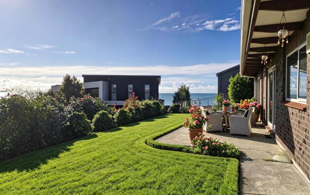 a backyard with a lawn and a house at Clifftop Coastal Retreat with Ocean Views - Close to Beach & Cafés in Auckland