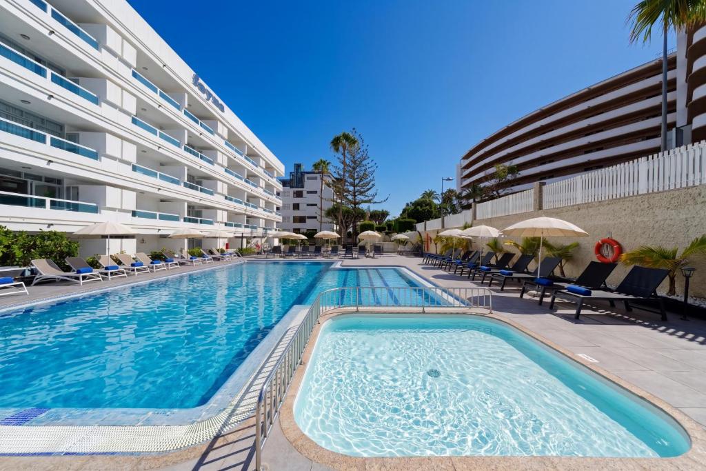 a swimming pool with chairs and umbrellas next to a building at Fayna Apartments in Playa del Ingles