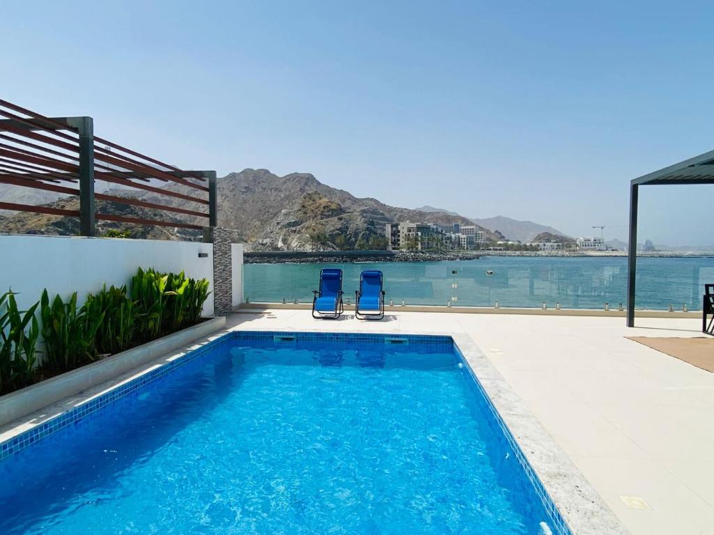 a swimming pool with two blue chairs next to the water at Al Dana H2O Beachfront Villa with a private pool, Al Dana Island Sharm Fujairah in Sharm