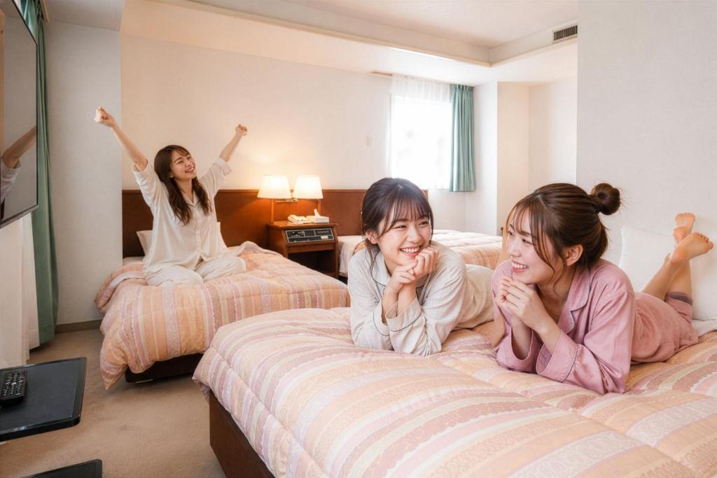 three girls laying on beds in a hotel room at Tendo Central Hotel in Tendo