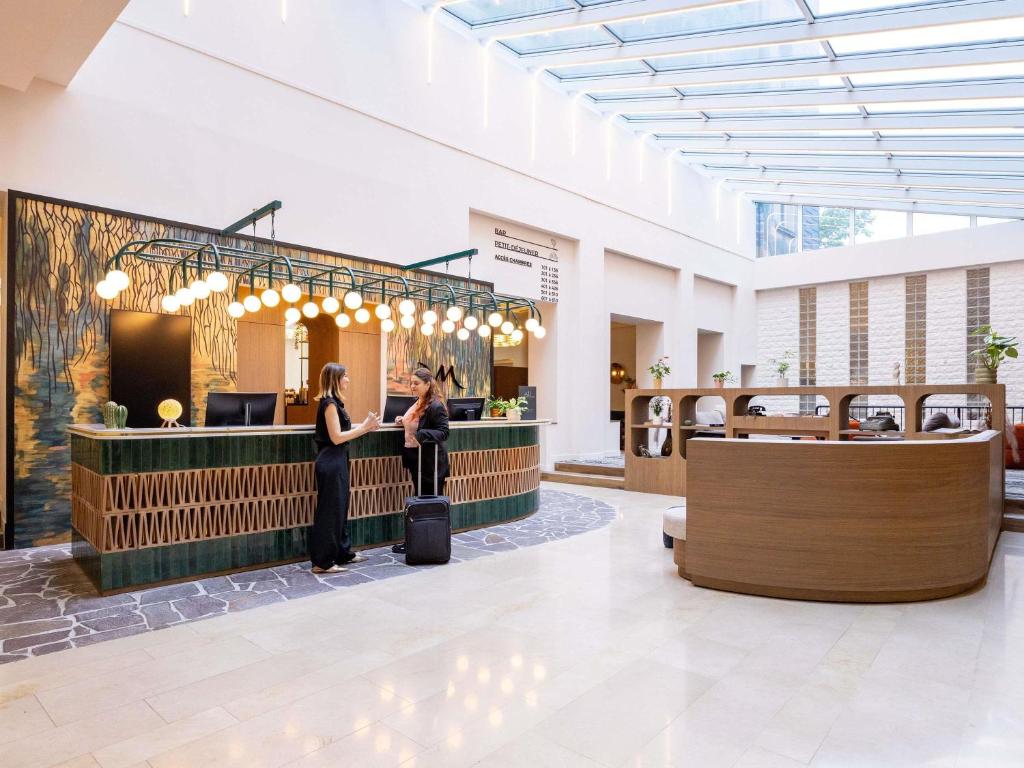 Eine Lobby mit zwei Frauen, die vor einem Tresen stehen. in der Unterkunft Mercure Brussels Centre Rogier in Brüssel
