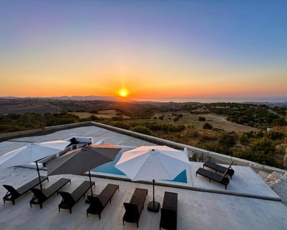 a patio with umbrellas and chairs with the sunset at Seaview Panorama Villa in Drousha
