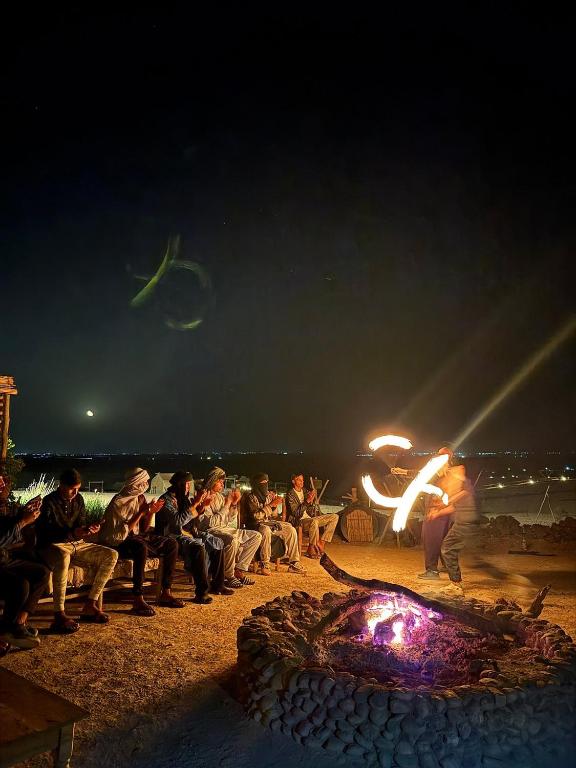 a group of people sitting around a fire pit at night at Caravansérail Agafay by Dar Inacamp in El Mjed
