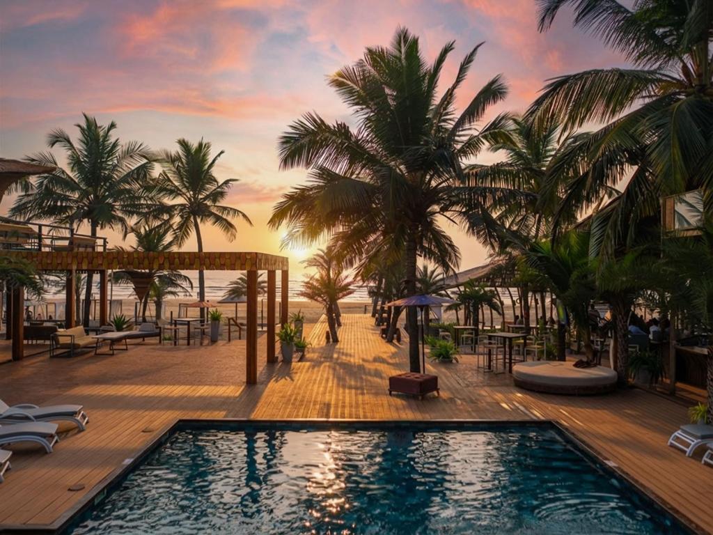 a resort pool with palm trees and a sunset at Marbela Beach Resort in Morjim