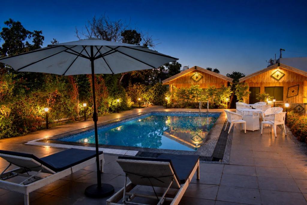 a swimming pool with an umbrella and chairs and a table at Gauri Hayat Corbett Retreat in Rāmnagar