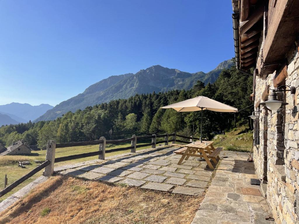 a table and an umbrella on a stone patio with mountains at Mountain hut 'la Fraccia' in Trasquera