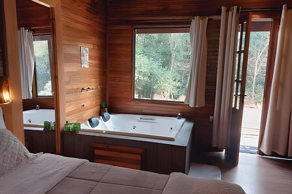 a bedroom with a tub and a bed and a window at Cabana surucuã in Três Coroas
