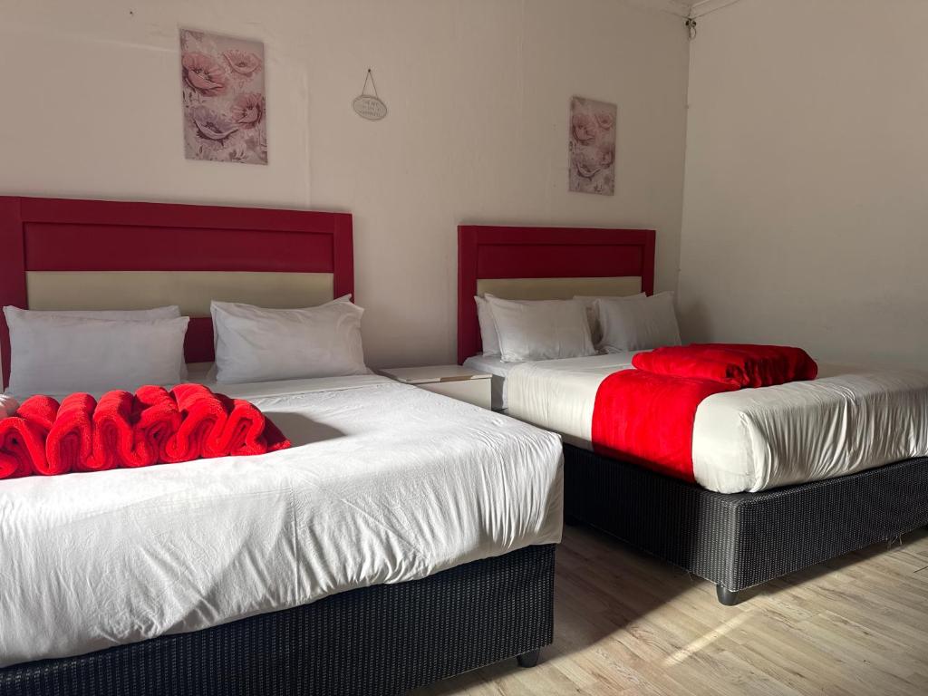 two beds with red sheets in a room at Aiden guest house in Gqeberha
