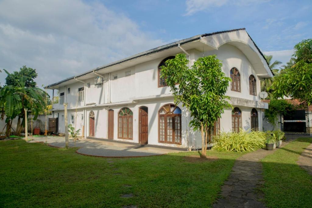 a white building with a tree in front of it at Sunshine Hotel in Hikkaduwa