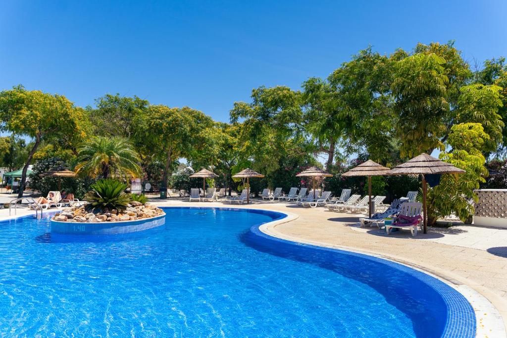 a swimming pool at a resort with chairs and umbrellas at Kampaoh Tavira in Tavira