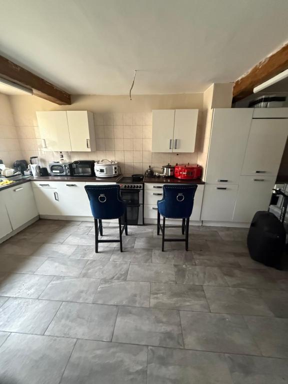a kitchen with white cabinets and blue chairs in it at Cottingley Spring farm house in Leeds