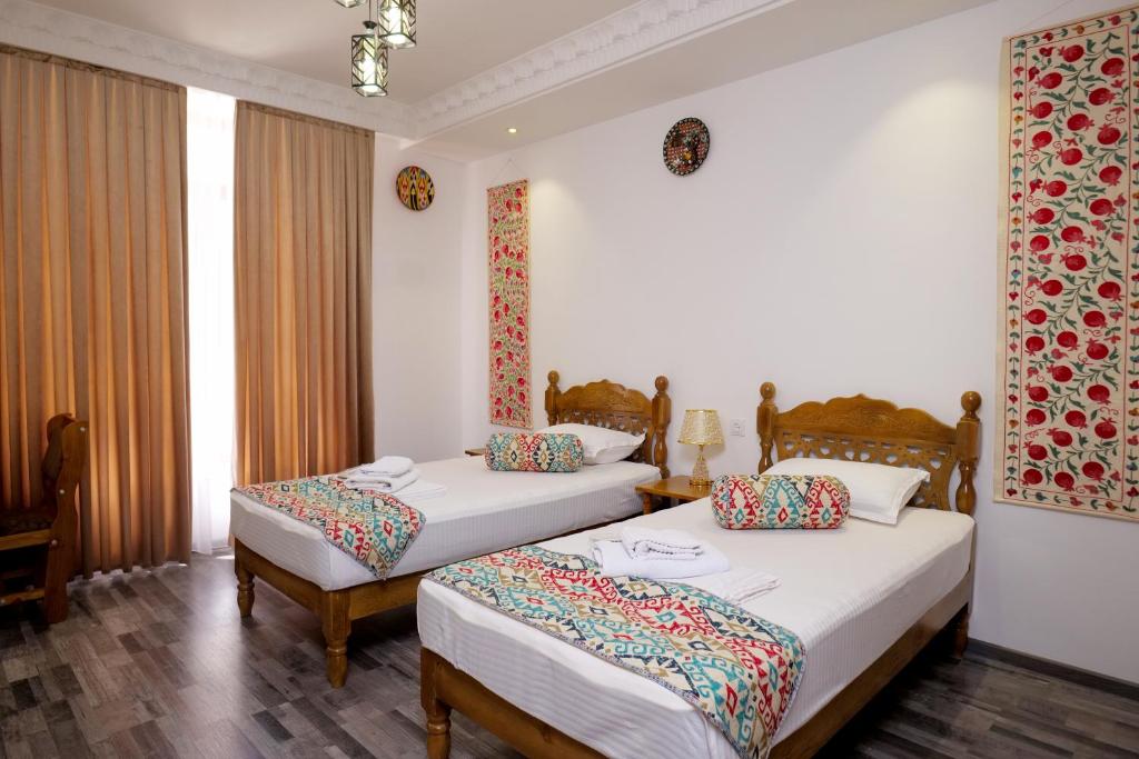 two beds in a hotel room with white walls at Mashkobi Buxoro in Bukhara